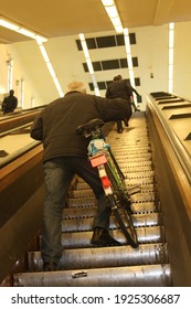 
People Going Up And Down The Escalator On Their Bikes In The Subway. One Person Also Carries His Bicycle.