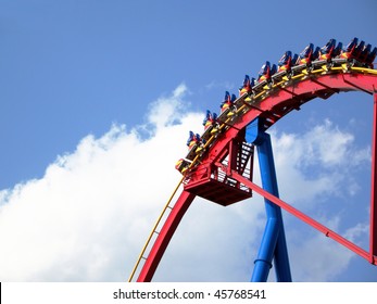 People Going Down On Giant Roller Coaster Ride, Photo Taken Against Bright Blue Sky And White Cloud