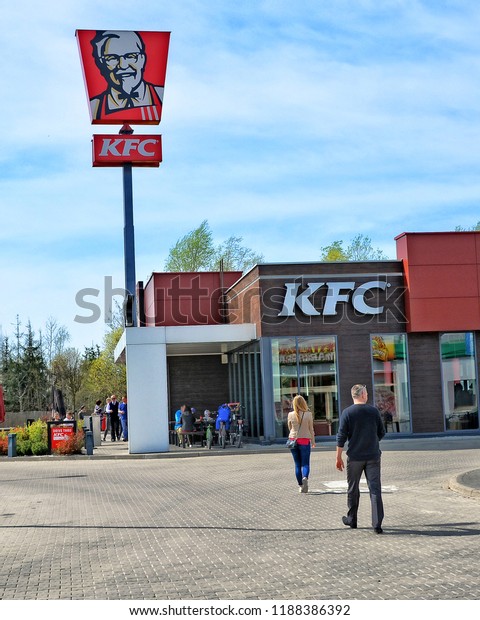 People going to KFC restaurant. Fast food restaurant\
chain on European roads. Red sign and logo of KFC. Poland, Warsaw –\
April 15, 2018 