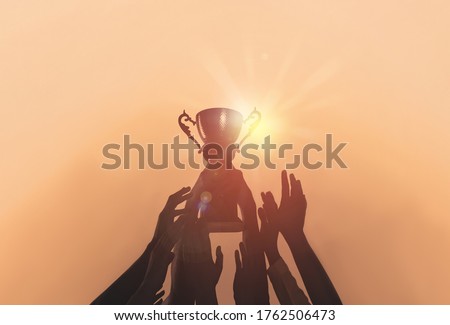 People with gold trophy cup on color background, closeup
