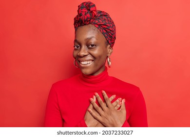 People gratitude and thankfulness concept. Pleased Afro American lady presses hands to heart expresses tender feelings says thanks for compliment appreciates something admires so sweet scene