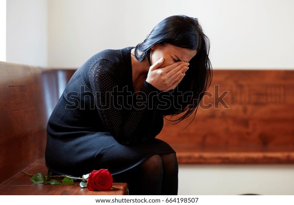 people, grief and mourning\
concept - crying woman with red rose sitting on bench at funeral in\
church