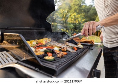 People grilling fish and corn on a modern grill outdoors at sunet, close-up. Cooking food on the open air