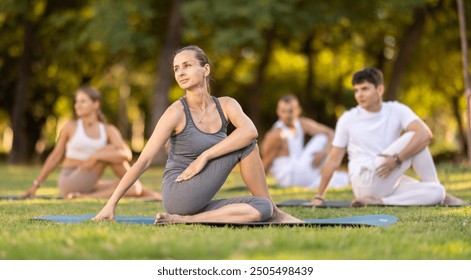 People group in park practicing yoga outdoor. Active pastime together, performing gymnastic exercise. Yoga lesson visitors and coach do lord of fishes. People practice sports during yoga in nature - Powered by Shutterstock