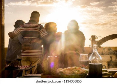 People Group Of Senior Friends Hug And Celabrate Together Viewing The Golde Sunset From A Rooftop Terrace. Living Always In Vacation And Retired Happiness Concept. Dinner And Food On The Table To Make