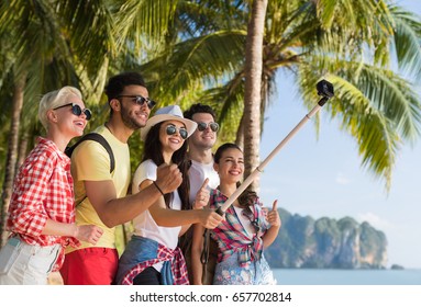 People Group Take Selfie With Action Camera On Stick While Walking In Palm Tree Park On Beach, Happy Smiling Mix Race Friends On Summer Vacation
