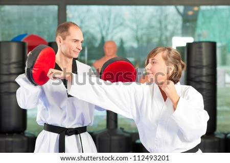 People in a gym in martial arts training exercising Taekwondo, both have a black belt