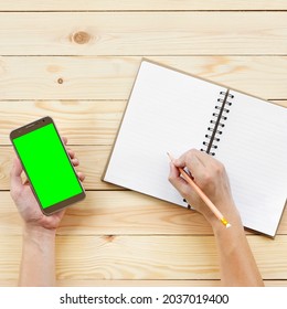 People Hand Holding Pencil And Watching Smartphone With Writing Diary Or Book On Top View Wood Table For Video Call Learning Or Study Online Included Clipping Path On Phone Display And Green Screen