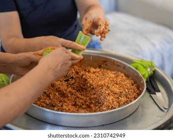 People hands are preparing food. Red Peppers, yellow tomatoes, white zucchini and grape leaves stuffed with minced meat. - Shutterstock ID 2310742949