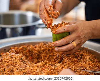People hands are preparing food. Red Peppers, yellow tomatoes, white zucchini and grape leaves stuffed with minced meat. - Shutterstock ID 2310742955