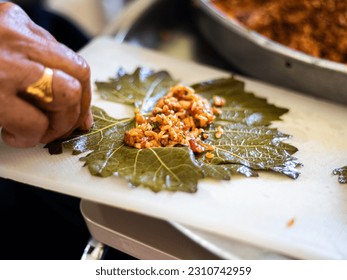 People hands are preparing food. Red Peppers, yellow tomatoes, white zucchini and grape leaves stuffed with minced meat. - Shutterstock ID 2310742959