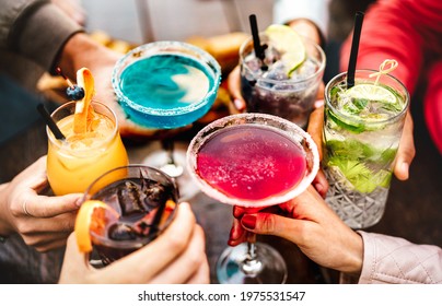 People hands toasting multicolored fancy drinks - Young friends having fun together drinking cocktails at happy hour - Social gathering party time concept on warm vivid filter - Shallow depth of field