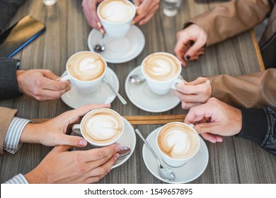 People hands view drinking cappuccino inside vintage cafeteria bar - Young friends doing a breakfast during winter season - Bonding and coffee warm beverage concept - Focus on bottom left hand - Powered by Shutterstock