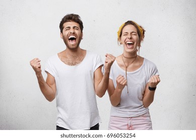 People, happiness, winning, victory, success and good luck. Indoor shot of two young Caucasian people man and woman expressing their excitement and delight by shouting Yes and clenching fists