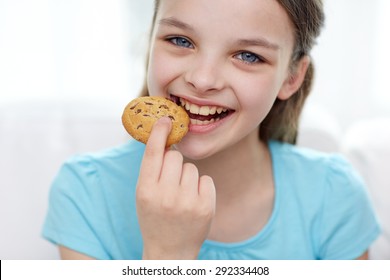 people, happy childhood, food, sweets and bakery concept - smiling little girl eating cookie or biscuit