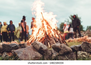 people having fun at the festival near camp fire with campfire song playing campfire games and eating camp fire grill, telling campfire stories near the fire with wood, flames in the nature