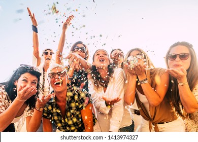 People having fun in party celebration friends concept - group of young and adult women all together laughing blowing coloured confetti - friendship and love for lifestyle with mixed active generation