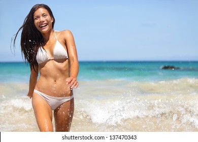 People having summer beach fun - woman in water smiling happy walking towards camera. Bikini girl on summer travel vacation on Hapuna beach, Big Island, Hawaii, USA. Multiracial Asian Caucasian woman.