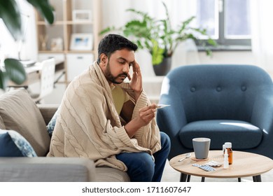 people, health and fever concept - sick indian man in blanket measuring temperature by thermometer at home - Shutterstock ID 1711607647