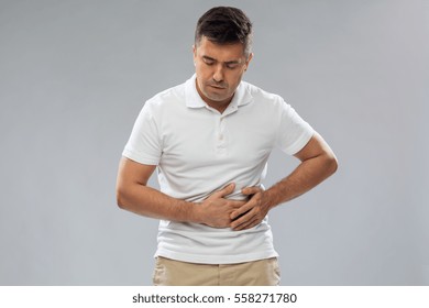 people, healthcare and health problem concept - unhappy man suffering from stomach ache over gray background