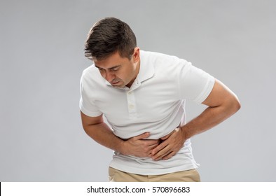 people, healthcare and health problem concept - unhappy man suffering from stomach ache over gray background