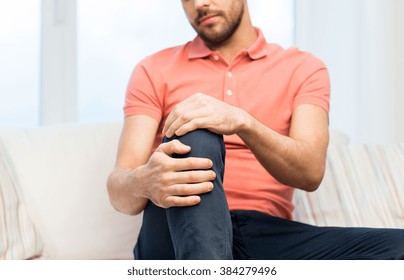 People, Healthcare And Problem Concept - Close Up Of Young Man Suffering From Pain In Leg Or Knee At Home
