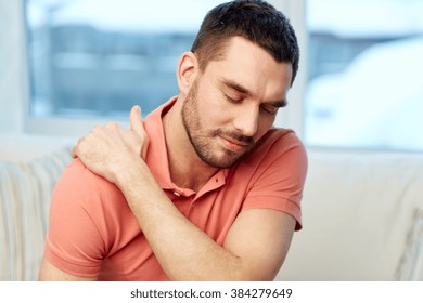 people, healthcare and problem concept - unhappy man suffering from neck or shoulder pain at home