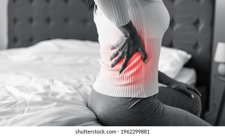 People, Healthcare and Treatment. Closeup of sick young African American woman suffering from acute side back pain, sitting on bed at home, touching area with red highlight. Black And White
