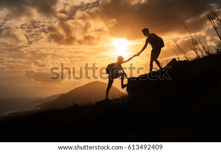 People helping each other concept. Man helping woman up the edge of a mountain. 
