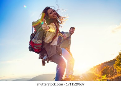 People Helping Each Other Hike Up A Mountain At Sunrise.