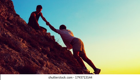 People helping each other hike up the mountain at sunrise. - Shutterstock ID 1793713144