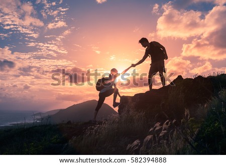 People helping each other hike up a mountain at sunrise.  Giving a helping hand, and active fit lifestyle concept.