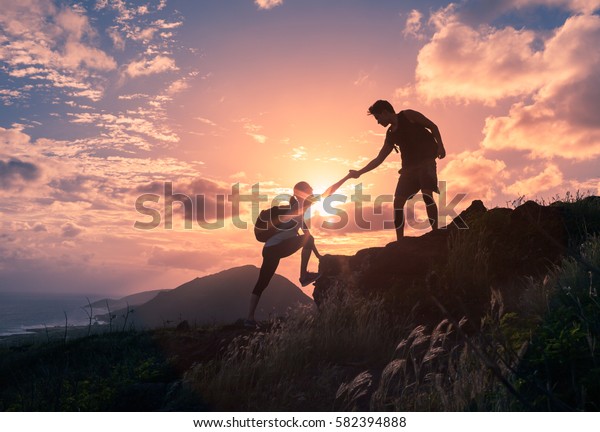 People helping\
each other hike up a mountain at sunrise.  Giving a helping hand,\
and active fit lifestyle\
concept.