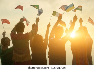 People holding different flags. Back view. Sunny evening sky background.