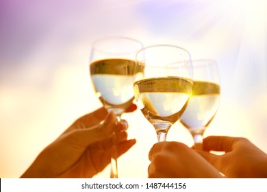 People holding Glass of Wine, Making a toast over Sunset sky. Birthday. Group of Friends drinking White Wine, toasting. Clink. Party outdoors. Enjoying time together. Holidays, vacation, celebrating
