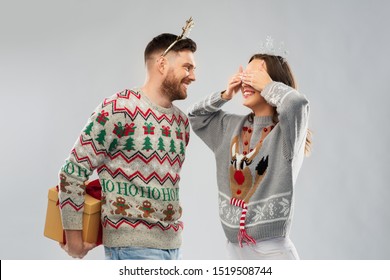 People And Holidays Concept - Portrait Of Happy Couple With Christmas Gift At Ugly Sweater Party