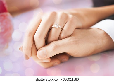 People, Holidays, Engagement And Love Concept - Close Up Of Engaged Couple Holding Hands With Diamond Ring Over Holidays Lights Background