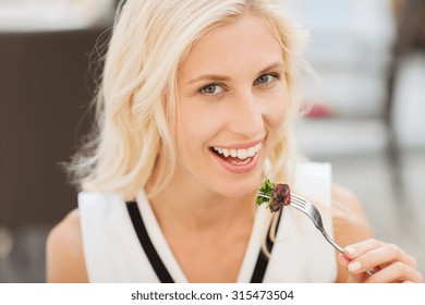 People, Holidays, Food And Leisure Concept - Happy Woman With Fork Eating Squid For Dinner At Restaurant Terrace