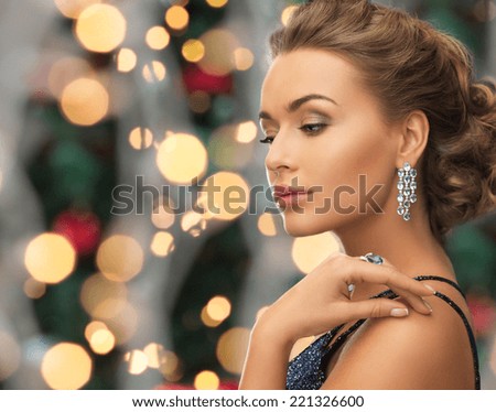 people, holidays and glamour concept - beautiful woman in evening dress wearing ring and earrings over christmas lights background
