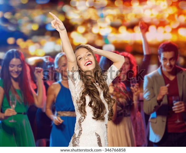people, holidays\
and nightlife concept - happy young woman or teen girl in fancy\
dress with sequins and long wavy hair dancing at night club party\
over crowd and lights\
background