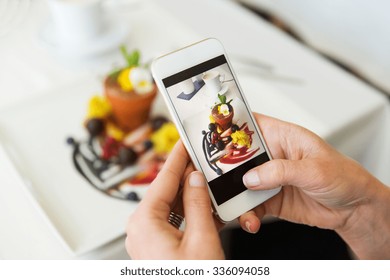 People, Holidays, Technology, Food And Lifestyle Concept - Close Up Of Woman With Smartphone Taking Picture Of Dessert At Restaurant