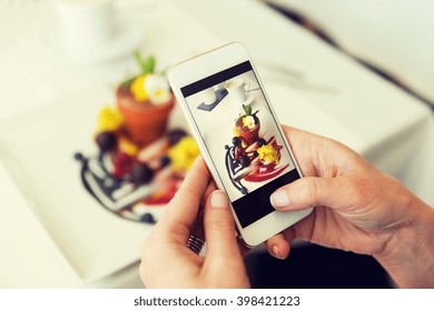 People, Holidays, Technology, Food And Lifestyle Concept - Close Up Of Woman With Smartphone Taking Picture Of Dessert At Restaurant