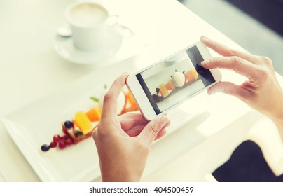 People, Holidays, Technology, Food And Lifestyle Concept - Close Up Of Woman With Smartphone Taking Picture Of Dessert At Restaurant