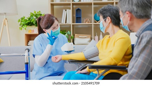 People Home Healthcare Concept - Asian Female Doctor Wearing Face Mask Is Using Blood Pressure Meter On Senior Woman While Elderly Man Take Care Of Her