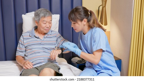 People Home Healthcare Concept - Asian Female Nursing Assistant Is Explaining Health Wearable Smart Watch To Senior Man Who Is Lying On Bed