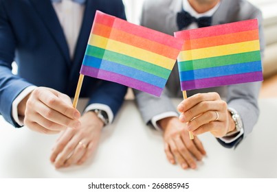 People, Homosexuality, Same-sex Marriage And Love Concept - Close Up Of Happy Male Gay Couple In Suits And Bow-ties With Wedding Rings Holding Rainbow Flags