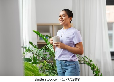 people, housekeeping and plants care concept - african american woman with houseplants drinking coffee at home - Shutterstock ID 1779702899