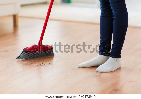 people, housework,\
cleaning and housekeeping concept - close up of woman legs with\
broom sweeping floor at\
home