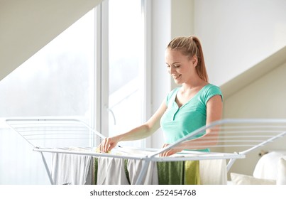 People, Housework, Laundry And Housekeeping Concept - Happy Woman Hanging Clothes On Dryer At Home