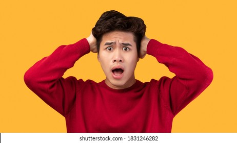 People, Human Emotions And Feelings Concept. Portrait of shocked scared asian man with open mouth grabbing head looking at camera in amazement, isolated over yellow studio background